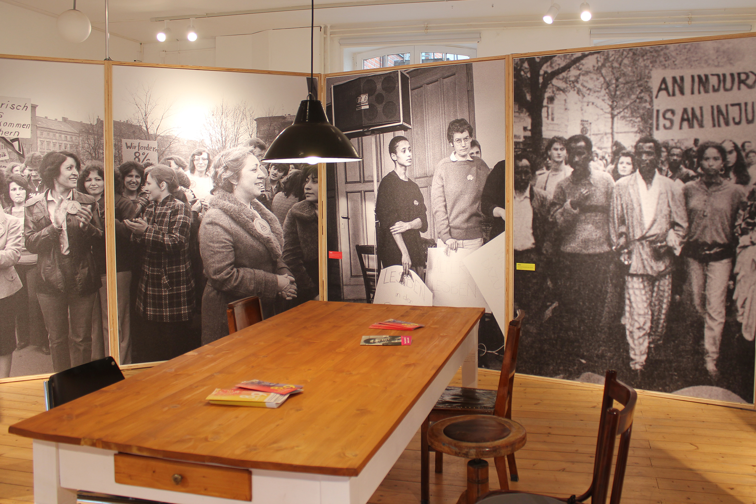 Großer Holztisch mit Stühlen in einem Raum, umgeben von schwarz-weißen historischen Fotografien von Menschen bei Demonstrationen.