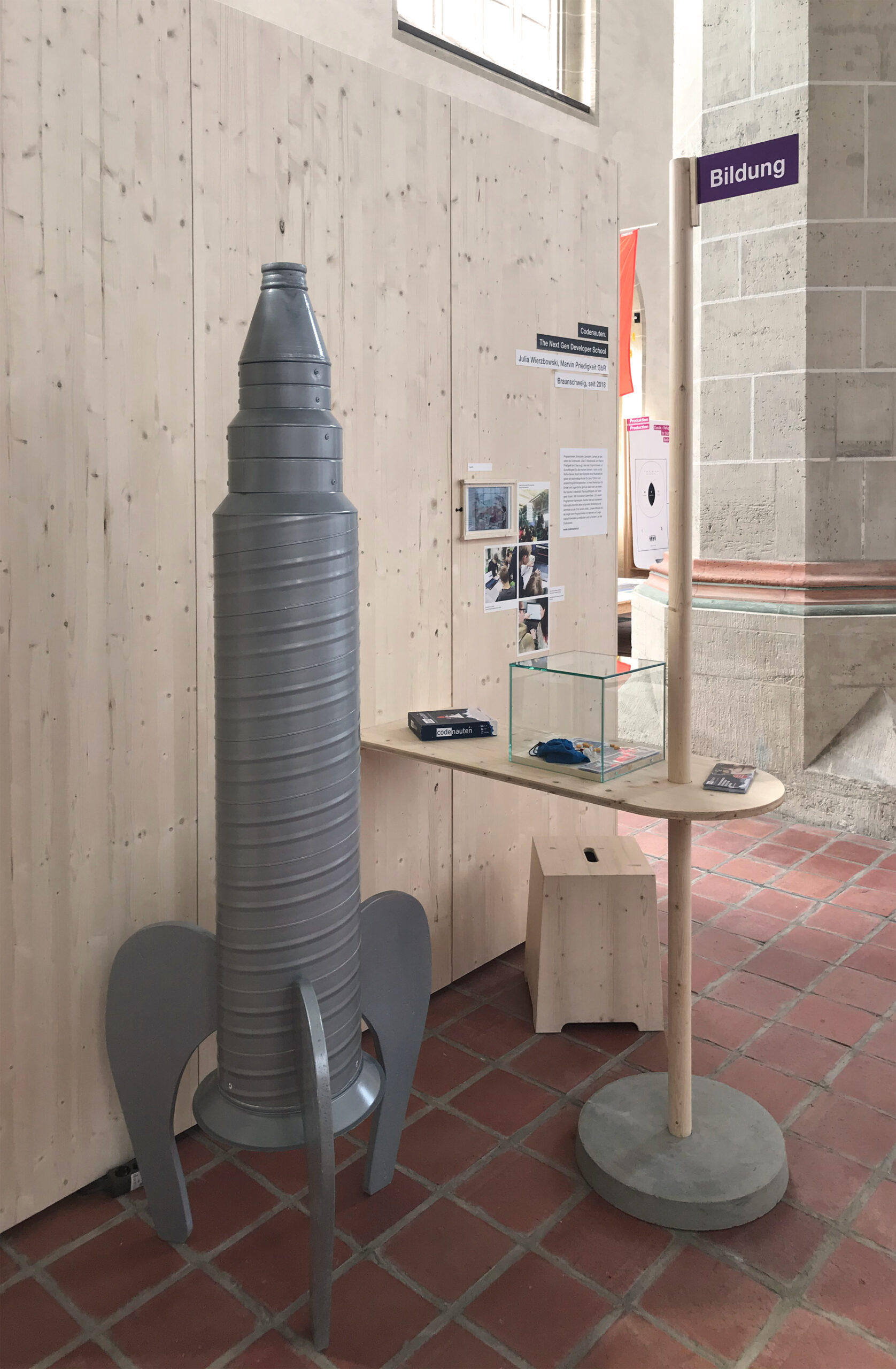 Station zum Thema Bildung mit grauer Raketenattrappe aus Metall mit dem Titel "Codenauten"