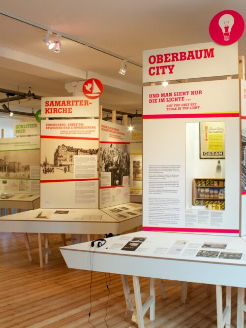 Ausstellungsraum mit mehreren Informationstafeln zu lokalenThemen, darunter "OBERBAUM CITY" und "SAMARITER-KIRCHE", auf Holzpodesten und mit Texten und Bildern.