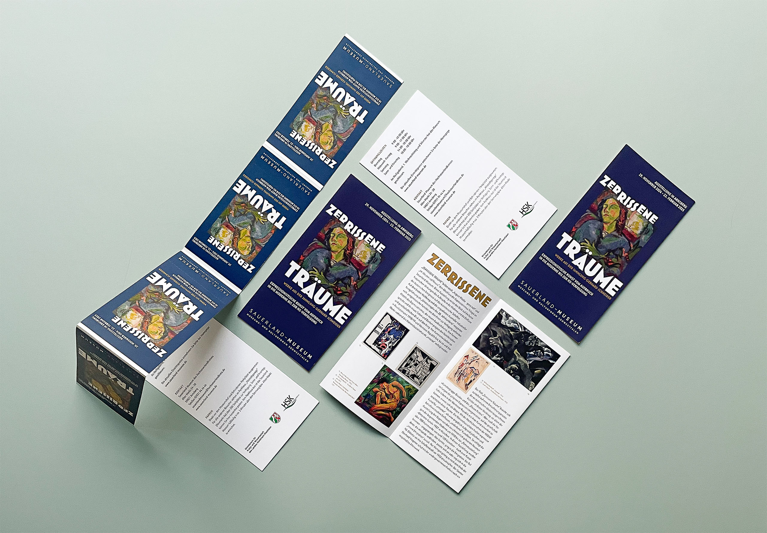 Ausstellungsflyer liegen und stehen mosaikhaft nebeneinander. Aussicht auf Leitmotiv. Ebenso sichtbare Rückseite mit Adresse, Öffnungszeiten, Preisen, Kontakt und Parkmöglichkeiten. Geöffneter Flyer mit Titel, dynamisch angeordneten Bildmotiven und Ausstellungsinformationen.